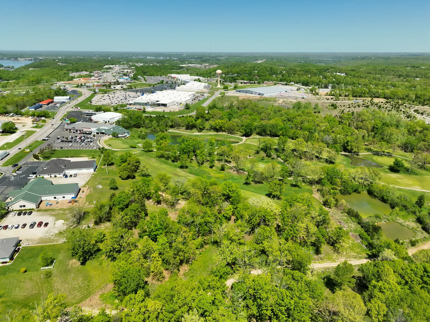 Aerial view over Osage Beach with commercial buildings, fairways, ponds, and wooded hills.