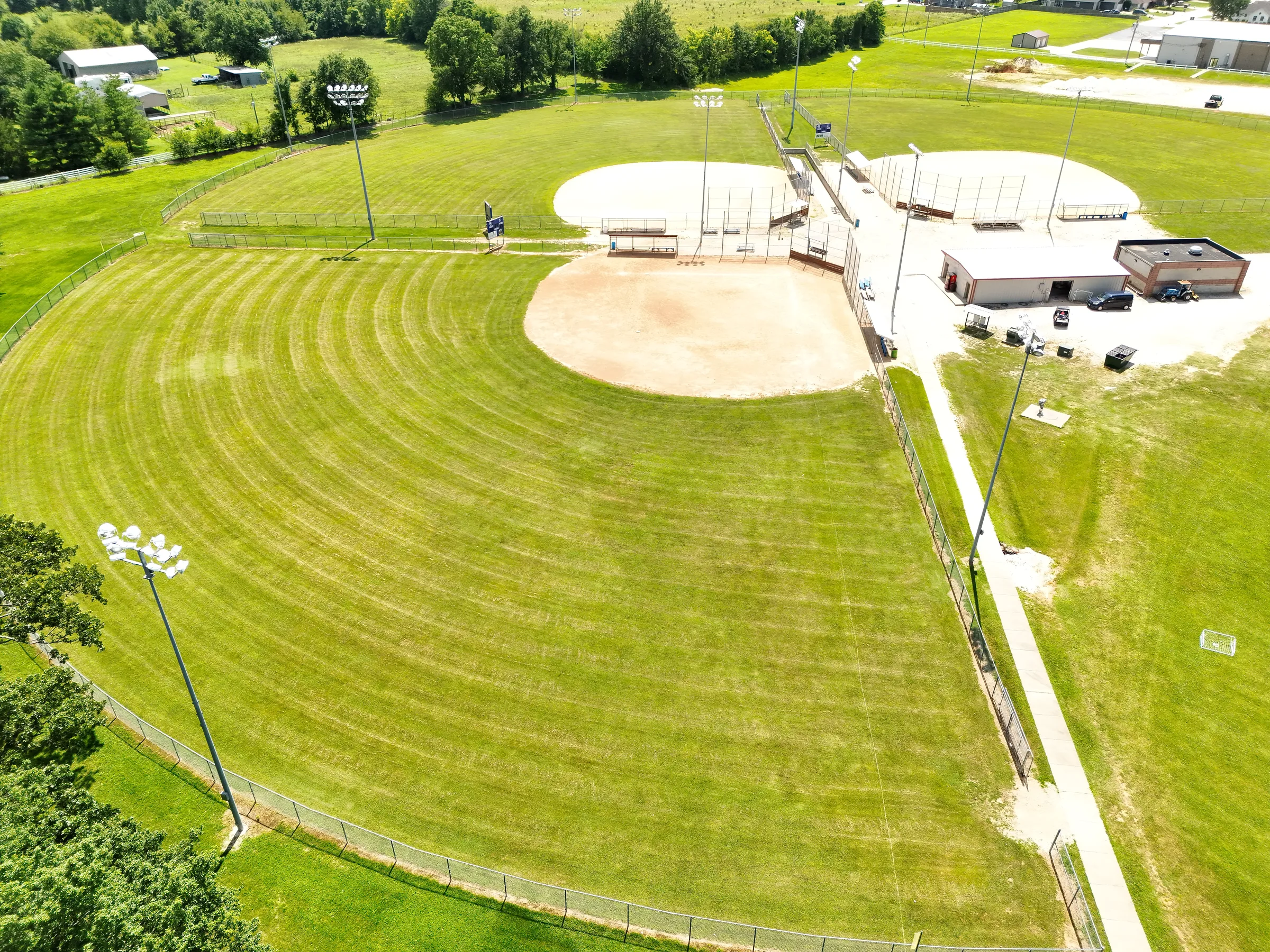 Oblique aerial view across a Fullerton Ball Fields outfield, infield, walking path, and central support buildings.