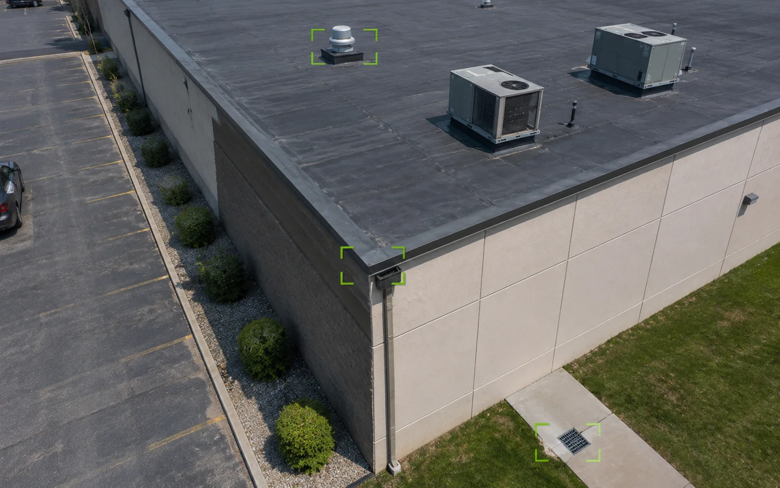 Illustrative aerial inspection view of a commercial building with subtle callouts around a rooftop feature, roof-edge drainage area, and site-access detail.