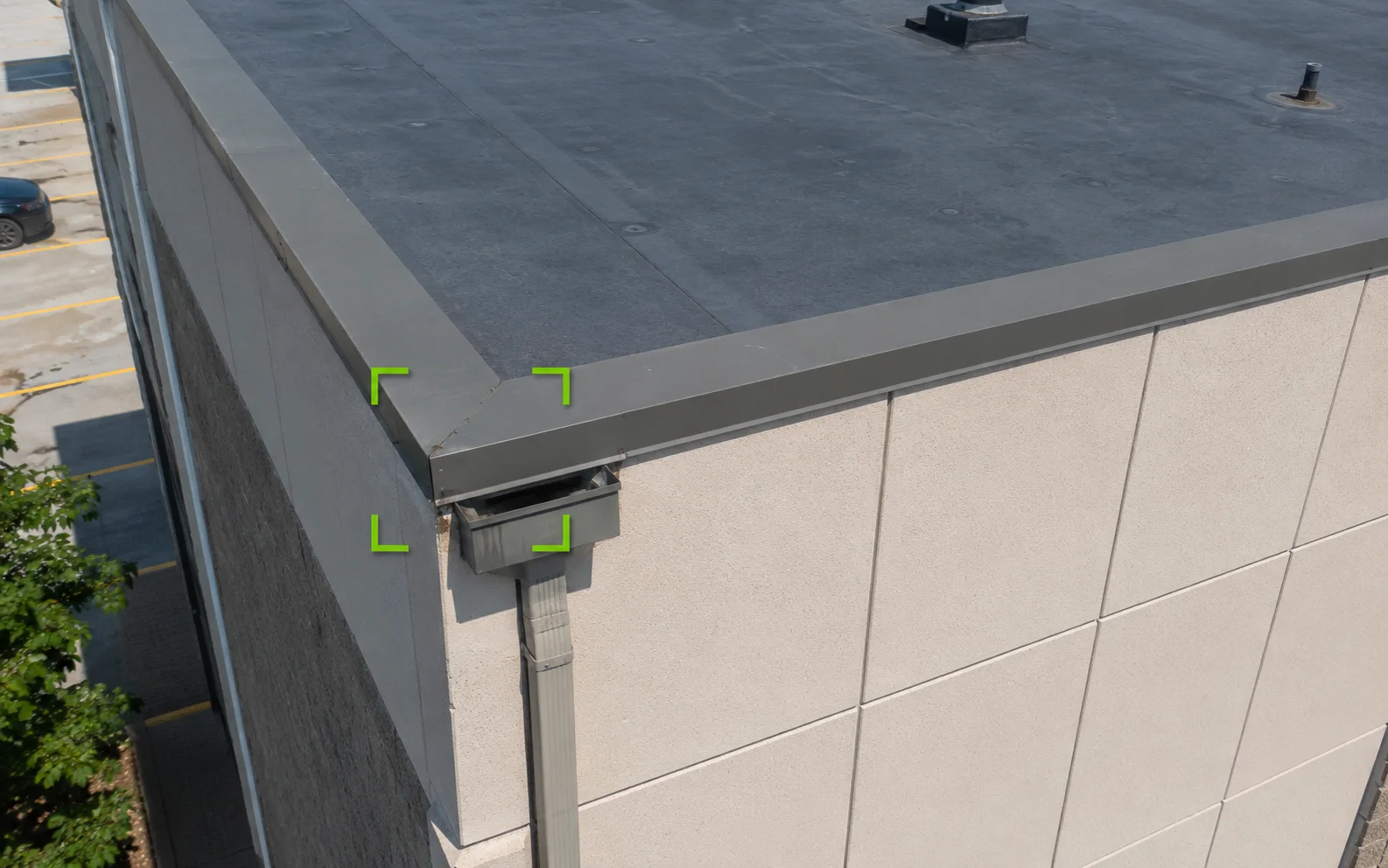 Illustrative close aerial detail view of a commercial roof edge, parapet cap, wall panels, and downspout area marked for follow-up review.