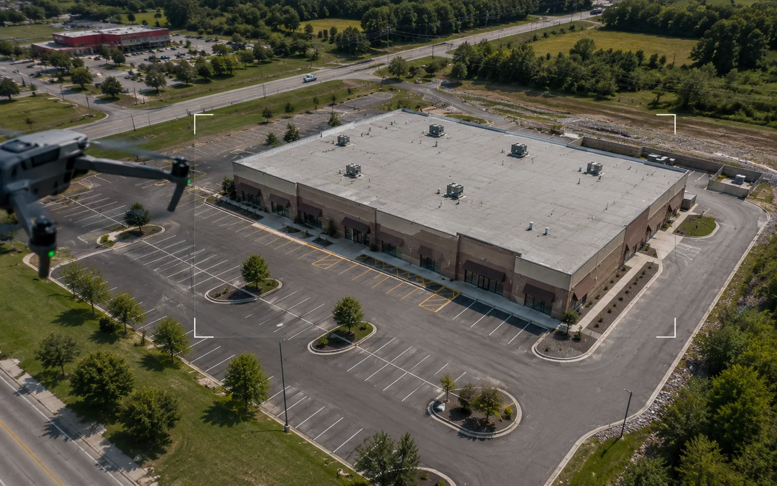 Illustrative scene of a drone capturing an overview image set of a commercial property, including the roof, parking areas, access lanes, and exterior context.