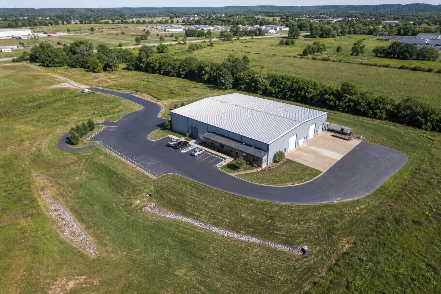 Illustrative aerial overview of a commercial property showing the building exterior, parking, loading access, perimeter, drainage path, and surrounding site context.